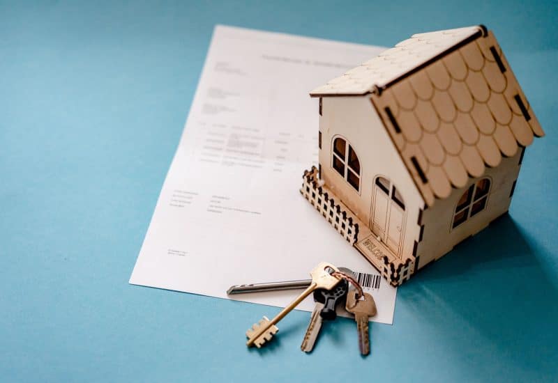 A photo shows a model house and a set of keys lying on top of a document perched on a table top.
