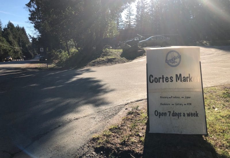 A sign indicates the driveway leading to a parking lot outside the Cortes Market general store.