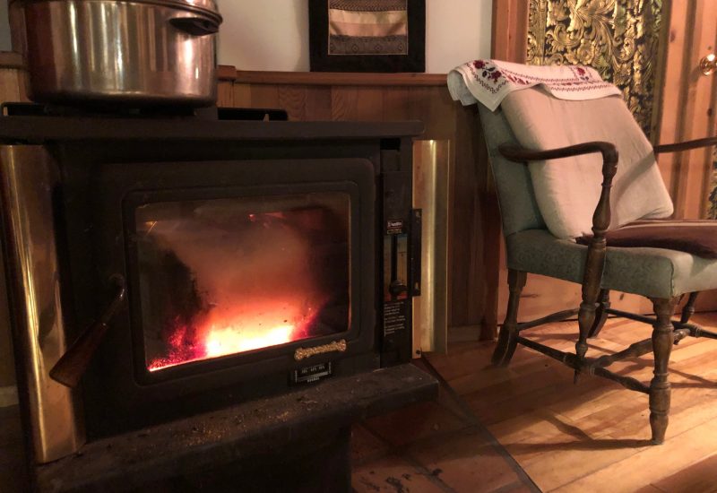 Black wood stove with a fire burning and an arm chair featured in a rural living room.