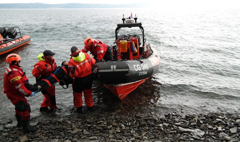 Three coast guards are training how to safely lift someone on a stretcher onto a rigid hull inflatable boat.