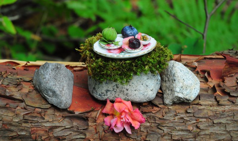 A fairy-size plate of food is nestled on a stone table on a log.